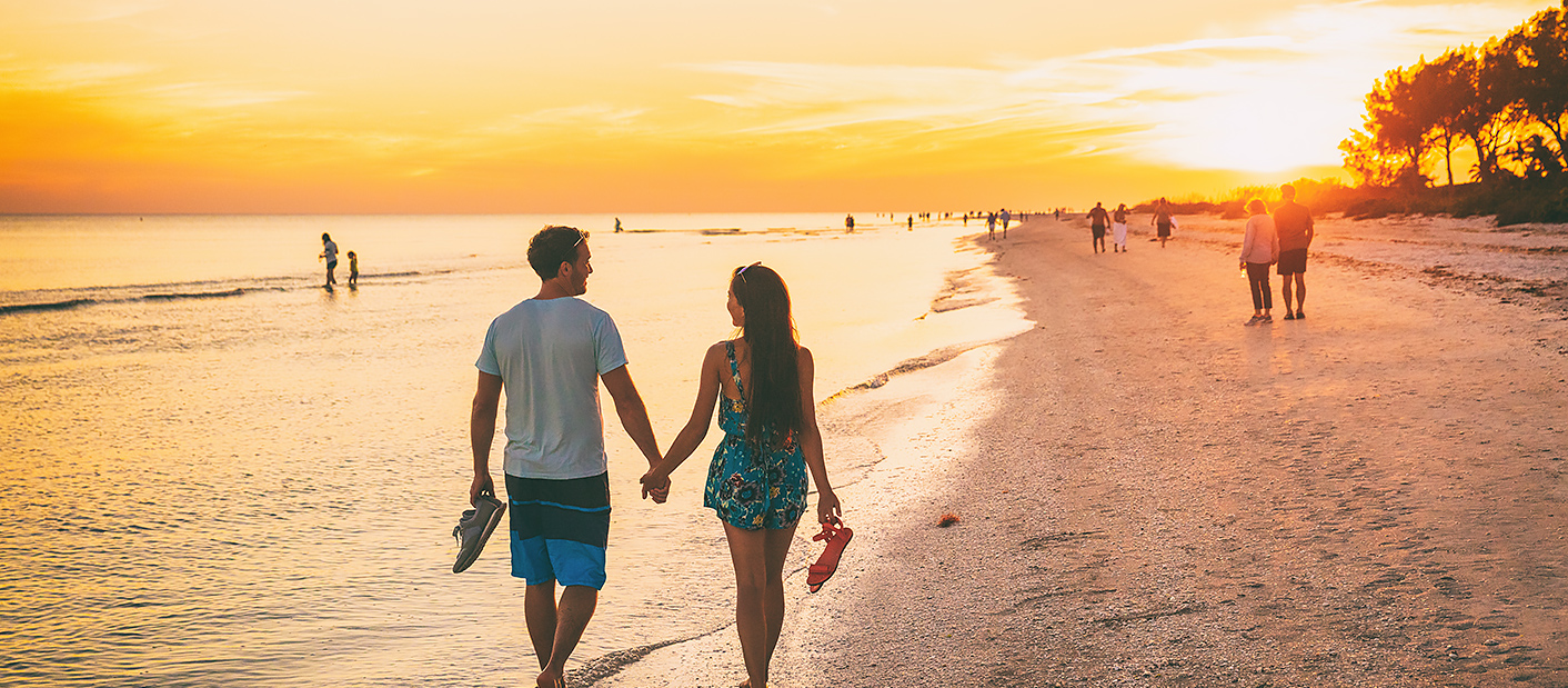 Couple walking hand-in-hand on the beach toward a beautiful sunset.