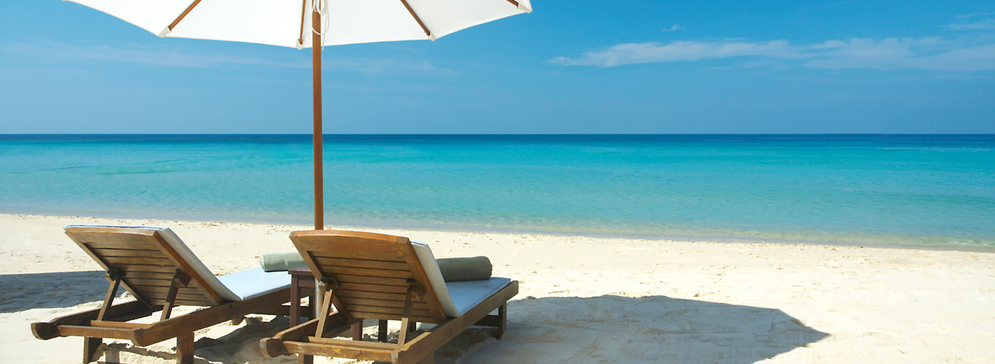 Two beach chairs under umbrella overlooking a beautiful beach