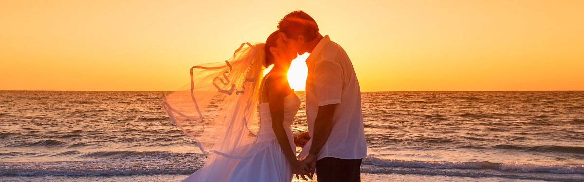 Newlyweds kissing in front of beautiful beach sunset