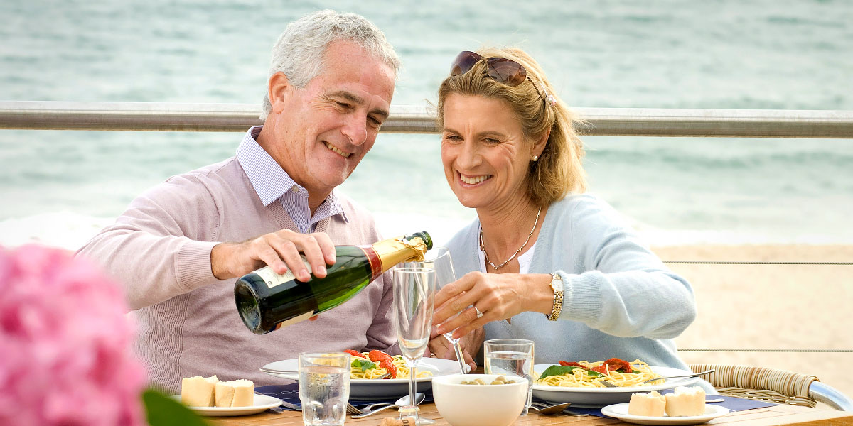 Happy mature couple pouring wine overlooking the beach