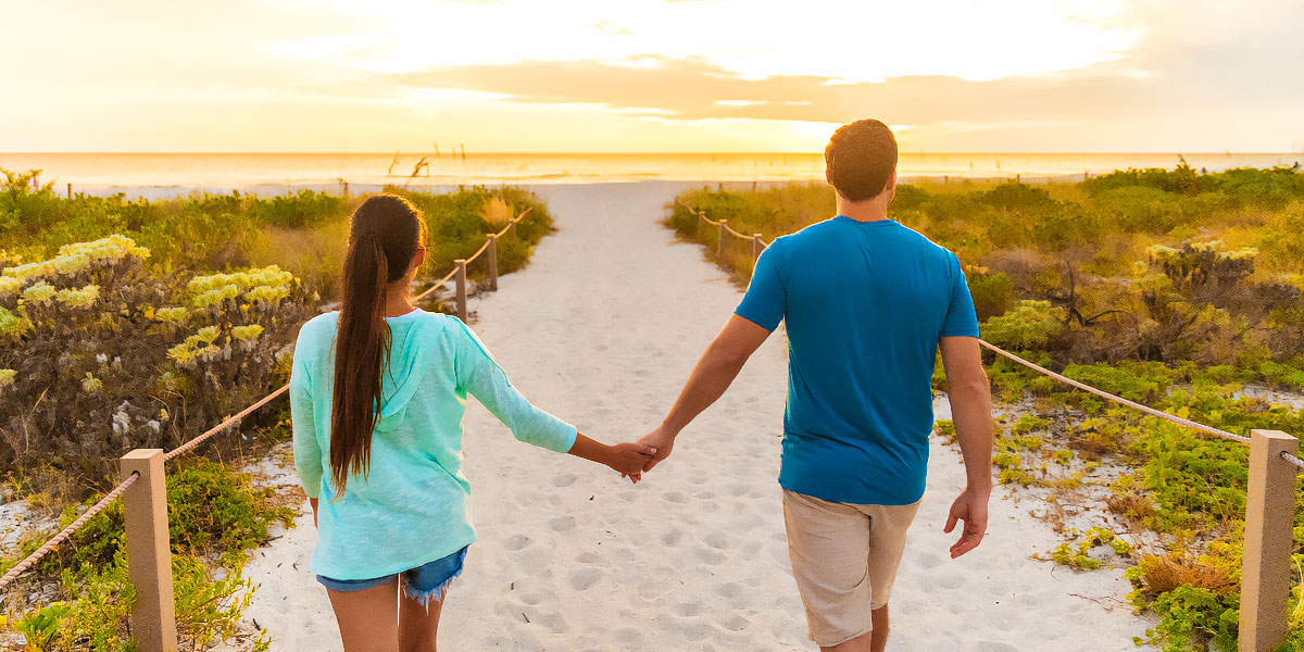 Couple holding hands walking toward beach at sunset